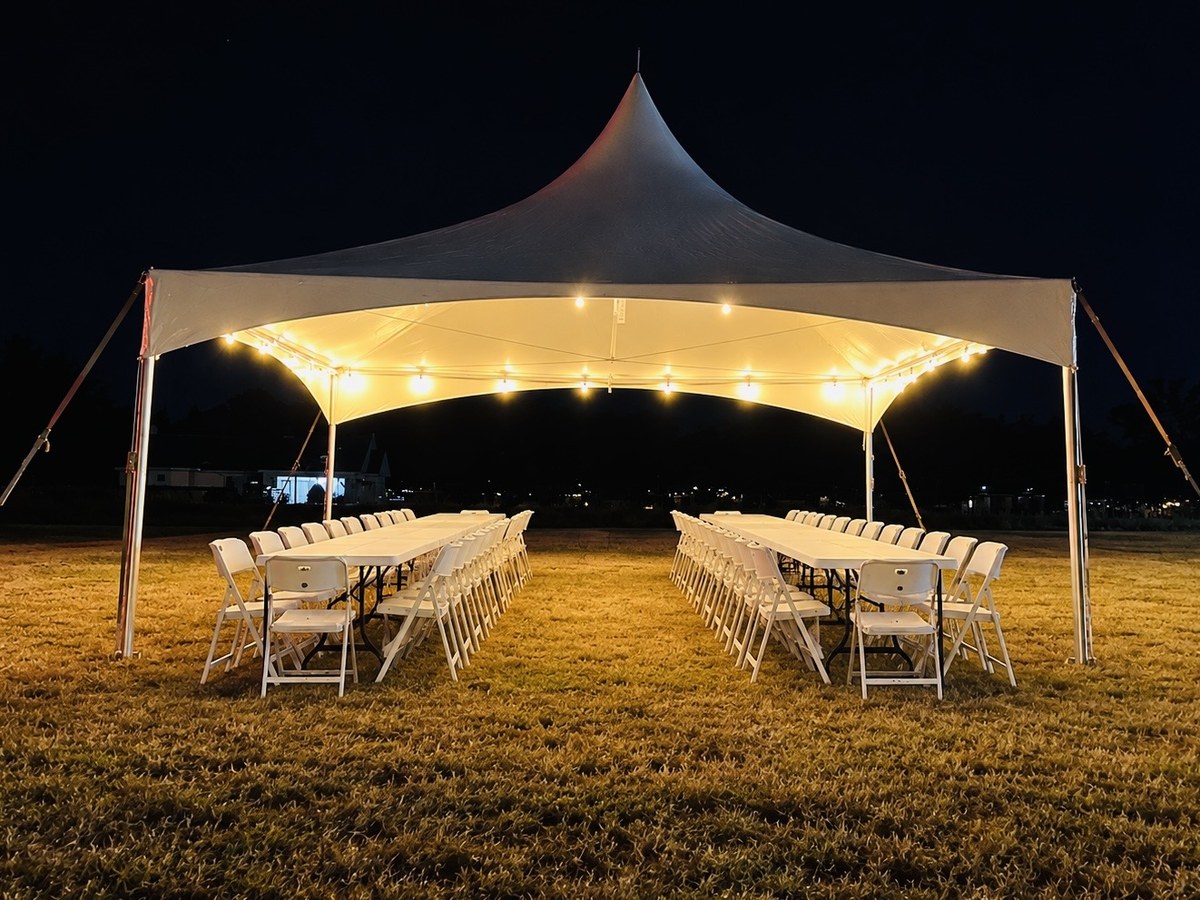 High Peak tent with banquet tables and white chairs at night